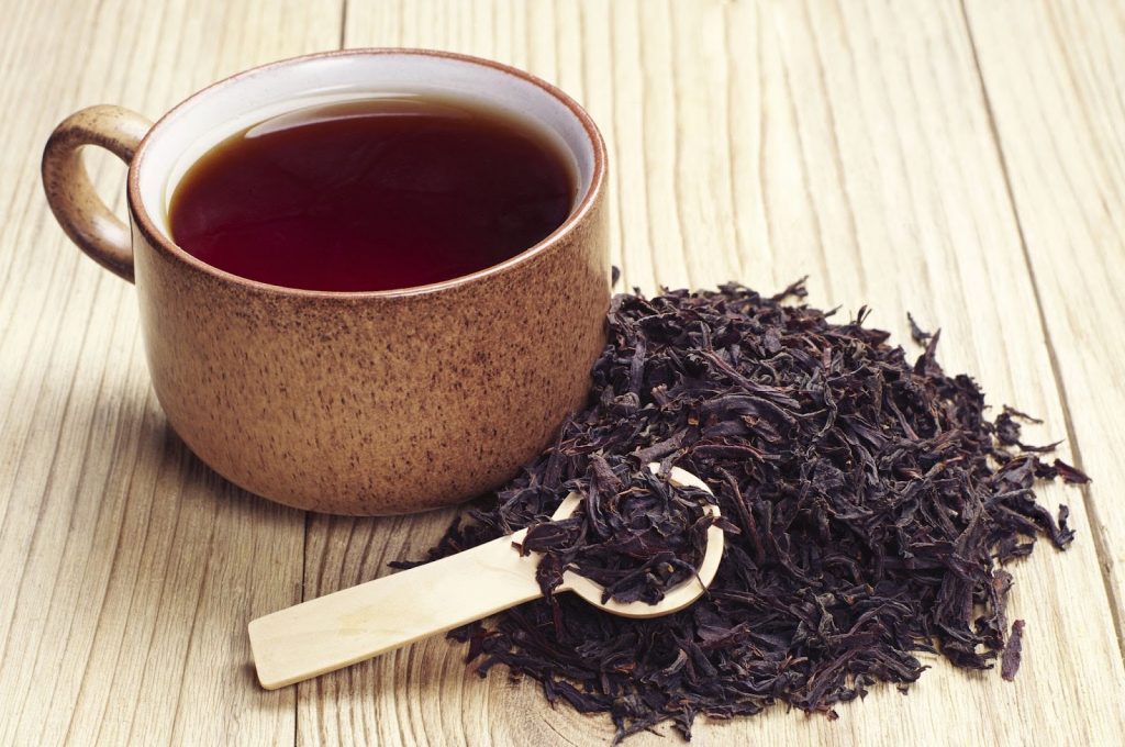 Black tea in a cup and dried leaves on wooden background